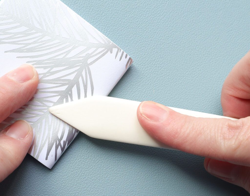 showing the steps of stacking paper with card stock on top then folding in half and creasing with a bone folder