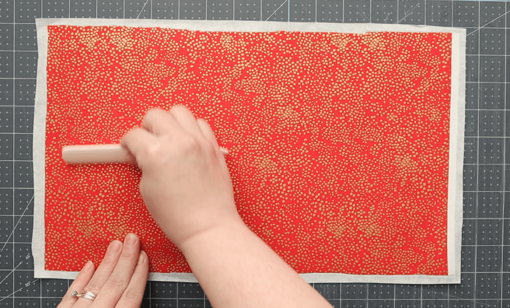hands applying paste to a cover board, then pressing the board down onto covering material and smoothing with a bone folder to remove excess air