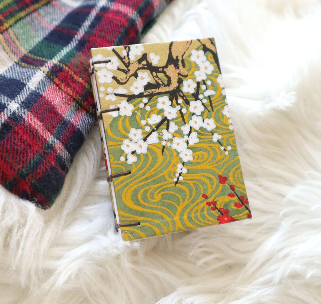 gold, red and white japanese chiyogami covered miniature coptic binding on a soft fluffy white and plaid christmas blanket