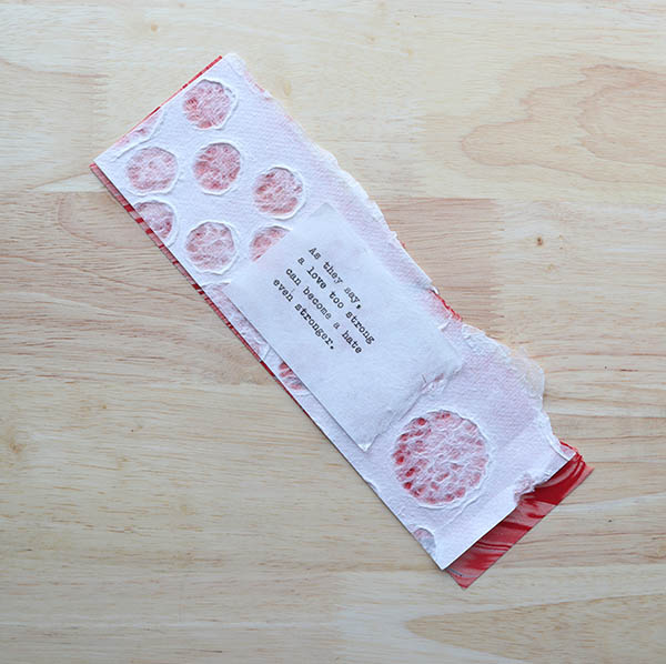 red marbled handmade paper layered underneath a strip of heavy mulberry paper embossed with stones layered under a typewritten verse on white paper